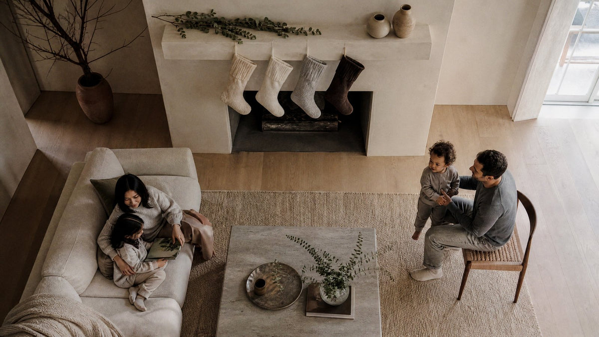 A restrained organic modern Christmas mantel with four neutral stockings in oatmeal, white, grey and dark brown on a plain plaster shelf