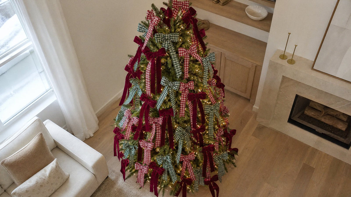 A Christmas tree densely decorated with red and green gingham check and burgundy velvet fabric bows in an ivory living room