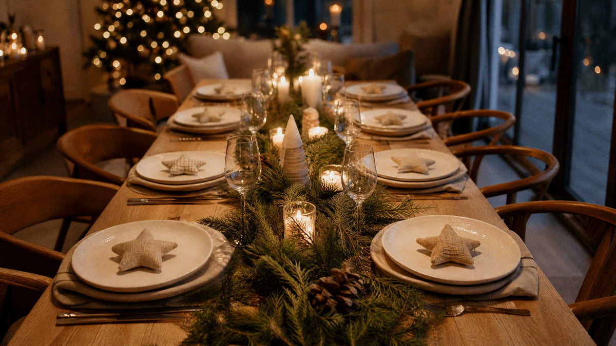 A Christmas dinner table where each place is set with a white plate and a small fabric star ornament used as a place marker, with cedar and candles down the centre
